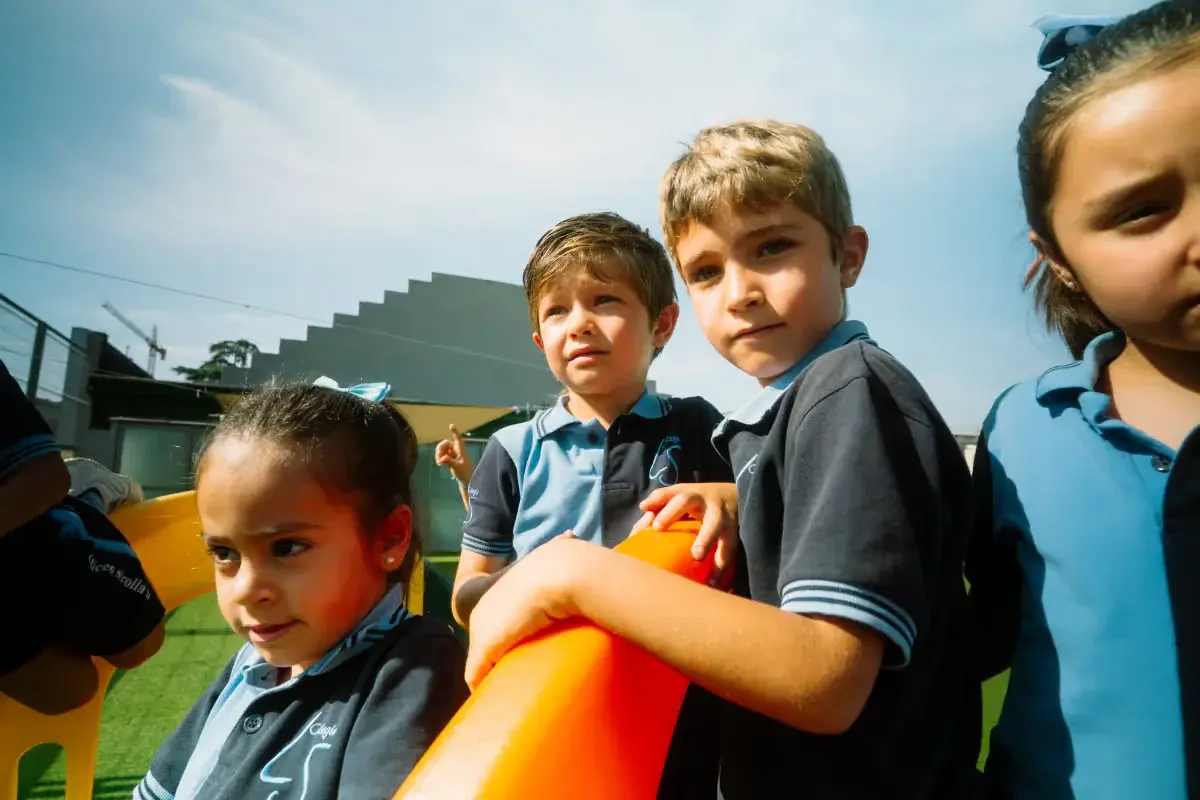 Niños jugando en estructura multicolor con toboganes en patio de escuela bajo sol brillante