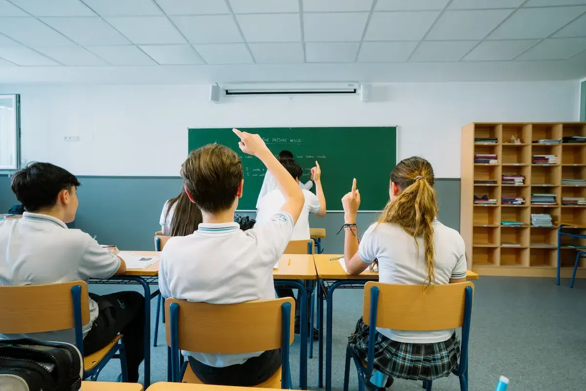 Docente guía a estudiantes de uniforme azul durante una clase colaborativa con materiales educativos en el aula
